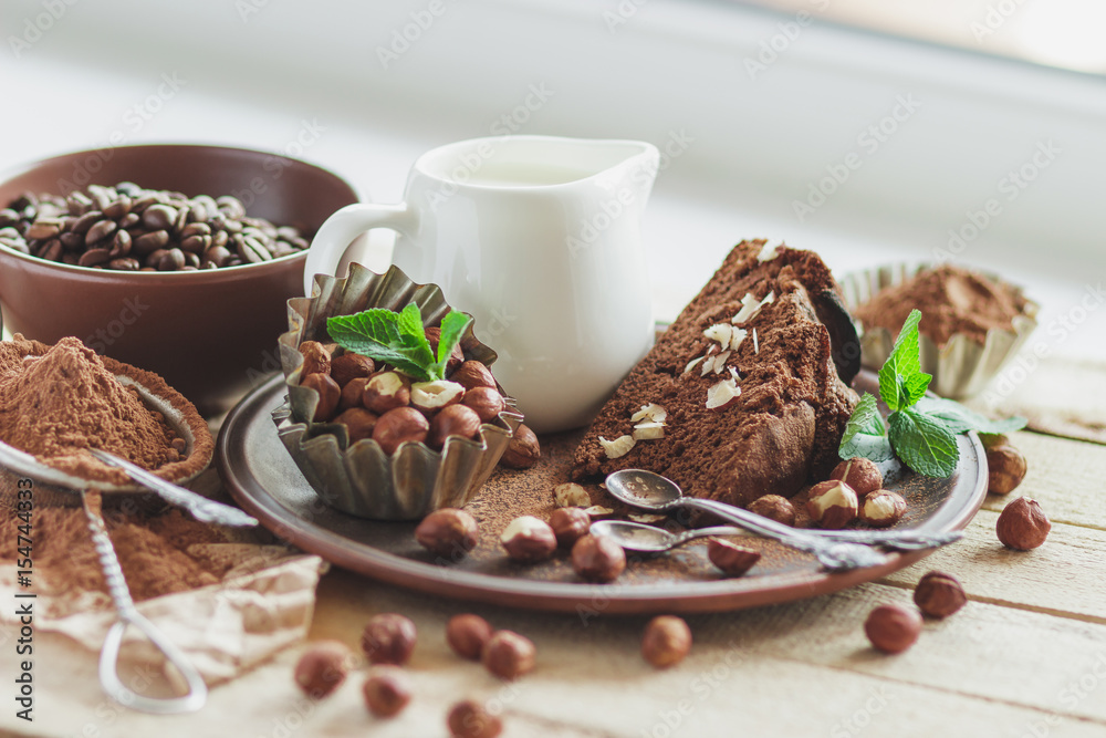 Piece of chocolate cake, mint leaves, hazelnuts and jar with milk Piece of chocolate cake, mint leaves, hazelnuts and jar with milk