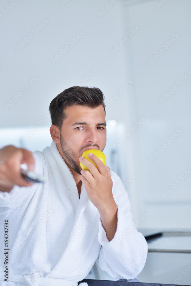 Young man in bathrobe sitting on kitchen worktop and having a cup of tea Young man in bathrobe sitting on kitchen worktop and having a cup of tea