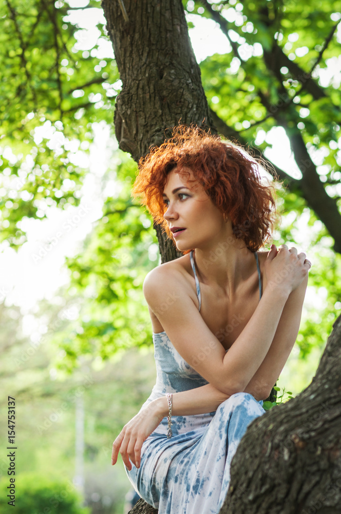 Photo of a beautiful redhead woman or girl sitting in the tree and watching the sunset. Sunshine Photo of a beautiful redhead woman or girl sitting in the tree and watching the sunset. Sunshine