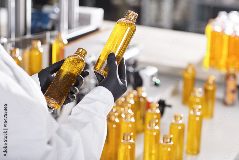 Manufacturing concept. Factory worker holding two glass bottles with yellow  liquid comparing quality between them. Factory process of production shampoo.  Technology, innovation and scientific concept Stock Photo | Adobe Stock