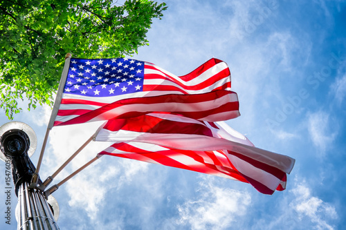 Three American flags attached to a light pole are waving in the breeze. Viewed from below looking up. Flags are back lit by sun. Beautiful sky. Location: Washington DC on Memorial Day