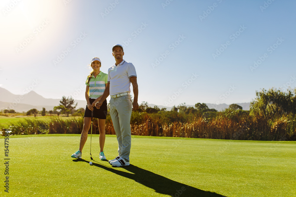 Male and female golfers at field on sunny day