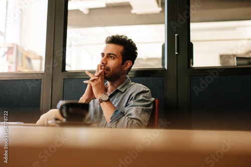 Photos Thoughtful young man sitting at table in conference room