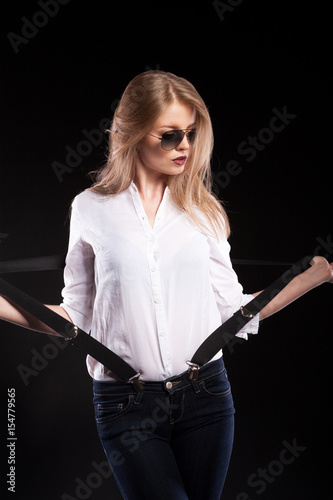 Sexy blonde model with suspenders and white shirt on black background in studio photo