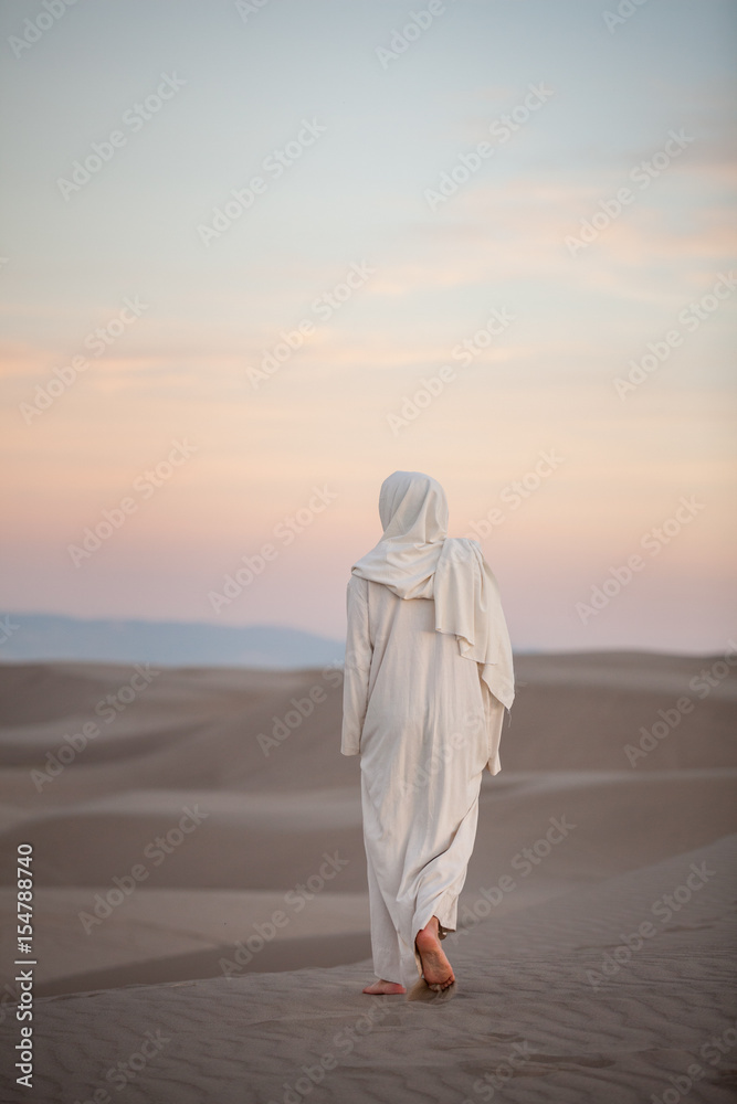 Jesus Christ walking through the sand at sunset with light pink and