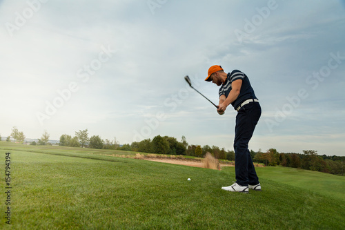 Golfer hitting iron club on golf course on fairway. Golf ball on tee.