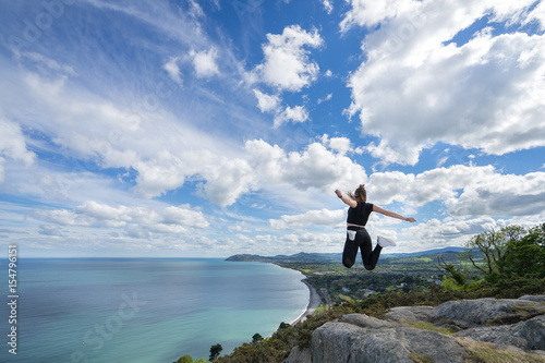 young beautiful girl female model photographer posing on top of the hill people embracing nature with open arms sea clouds blue sky tripod camera backpack sport clothes