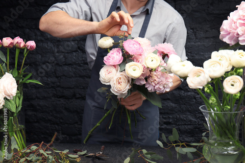 Male florist creating beautiful bouquet in flower shop, close up