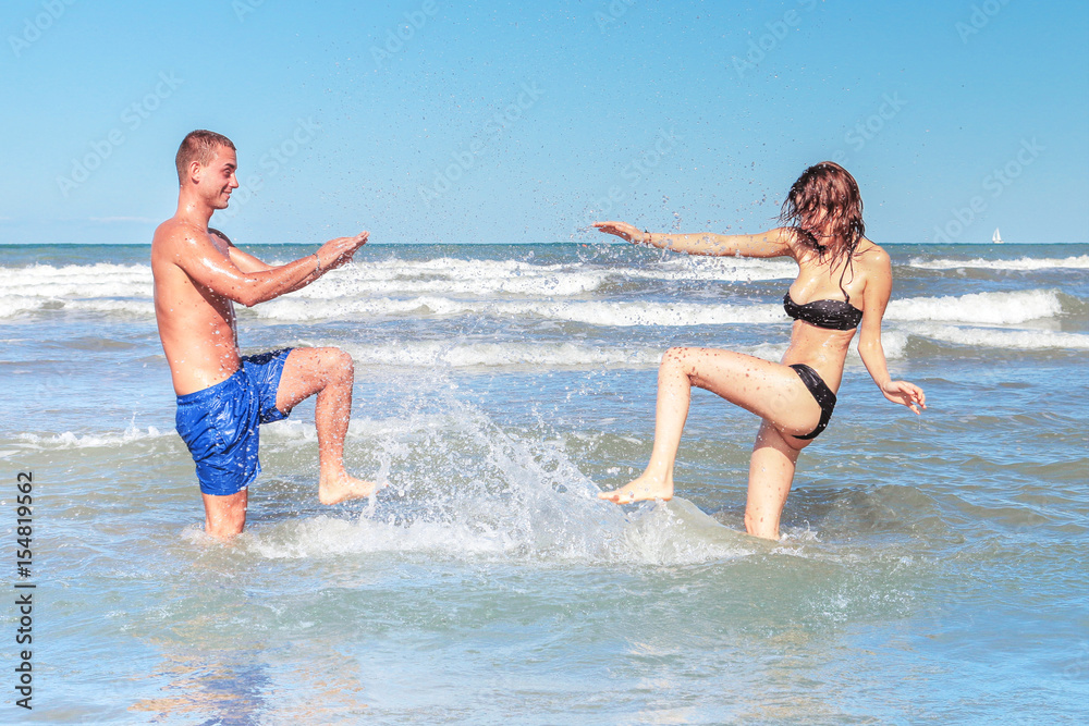 young couple playing splashing sea water on summer beach holiday. happy energetic girl and boy on active summer vacation on honeymoon concept young couple playing splashing sea water on summer beach holiday. happy energetic girl and boy on active summer vacation on honeymoon concept