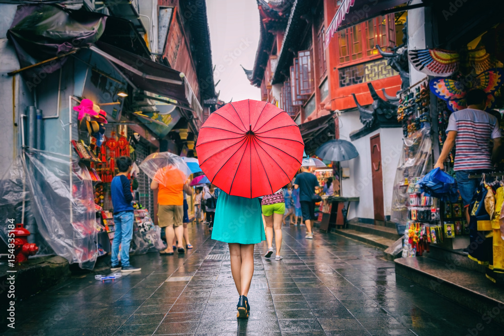 Naklejka premium Kobieta ludzi spaceru w chinatown ulicy handlowej. Deszczowy dzień dziewczyna turystycznych pod czerwonym parasolem orientalne w wąskich uliczkach na podróży w Chinach w Szanghaju.