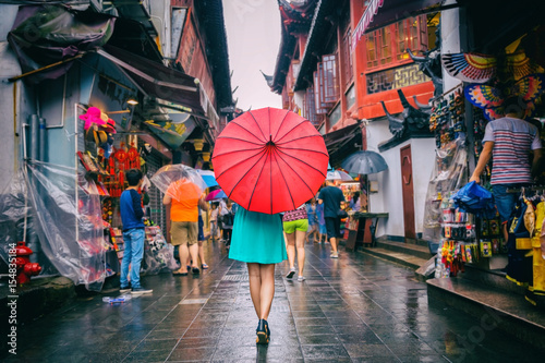 People woman walking in chinatown shopping street. Rainy day girl tourist under red oriental umbrella in narrow alleys on china travel in Shanghai. photo