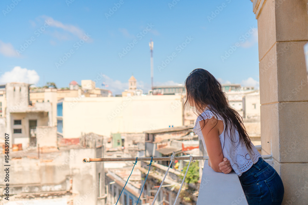 Young attractive woman on old balcony in apartment in Havana with vie of old town and houses