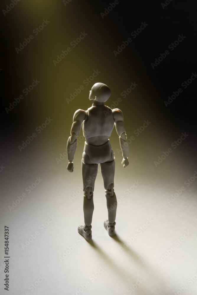 Man figurine standing in powerful pose looking up with beam of light illuminating it. Vertical conceptual image with copy space. Man figurine standing in powerful pose looking up with beam of light illuminating it. Vertical conceptual image with copy space.