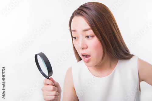 Young woman looking through a magnifying glass on a white background