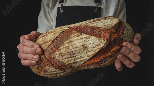 Baker's hands hold an oval bread.