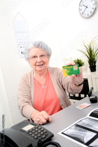 Senior woman in doctor's office showing carte vitale medical french social security card photo