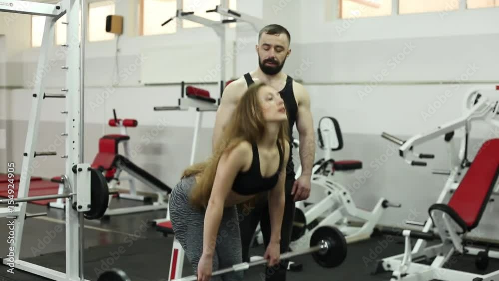 long-haired blonde woman in a black shirt and gray pants with a dark-haired bearded coach in a black shirt and gray pants work out tilts forward with dumbbells long-haired blonde woman in a black shirt and gray pants with a dark-haired bearded coach in a black shirt and gray pants work out tilts forward with dumbbells