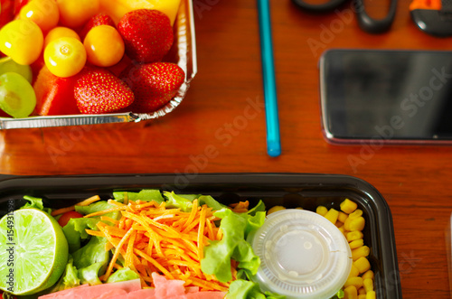 Close up of a delicious mediterranean-Style fresh salad with ham and fruit sal in a plastic box on wooden table photo