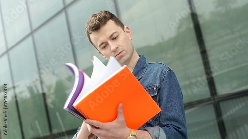 Young man standing next to the modern building and checking his notebooks, steadycam shot
 photo