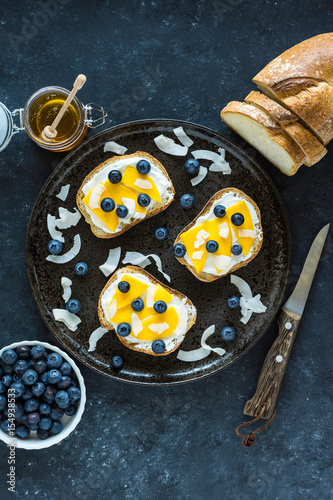 Sweet berry crostini sandwiches with ricotta mango blueberries and coconut chips on the whole grain bread