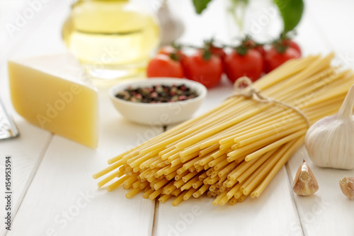 Dry pasta with cheese, tomatoes, garlic and oil on white wooden background.