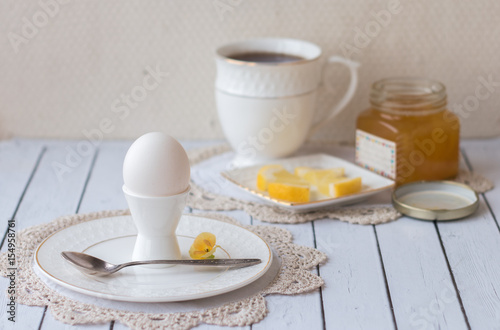 Beautiful Breakfast. Boiled egg white on a white stand for the eggs on a white plate on lace crochet doily. Tea in a white Cup  slices of lemon on a saucer  homemade lemon jam. Natural lighting.