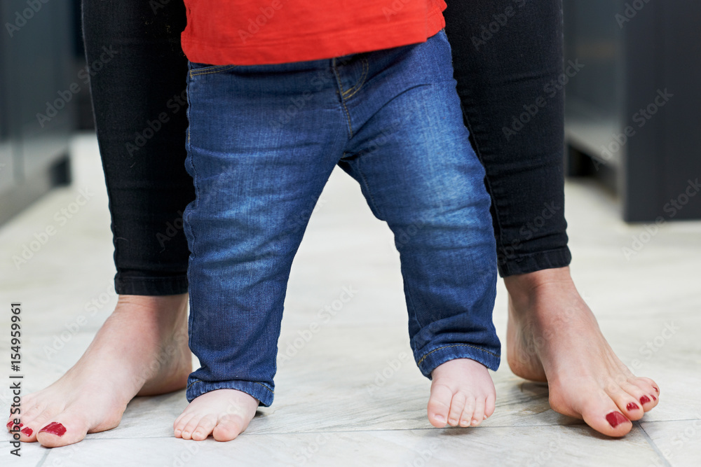 Close Up Of Mother Helping Baby Son To Walk In Kitchen Close Up Of Mother Helping Baby Son To Walk In Kitchen
