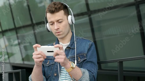 Stylish man standing next to the modern building and playing a game on smartphone, steadycam shot
 photo