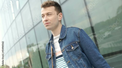 Stylish man smiling to the camera while standing next to the modern building, steadycam shot
 photo