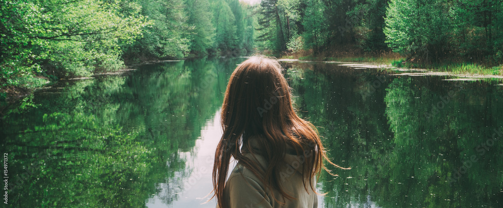 Naklejka premium dziewczyna stoi tyłem do aparatu. na tle pięknej rzeki. zielony las