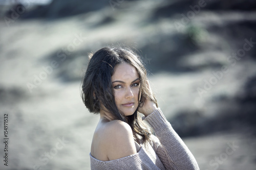 BeaBeautiful young brunette woman with sweater and shoulder bare in the sand on the beachutiful young brunette woman on the beach sand photo