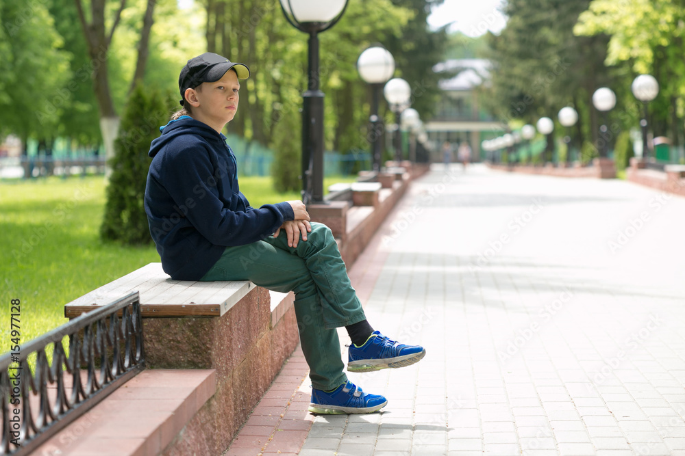 The teenager sits on a bench in a summer park.