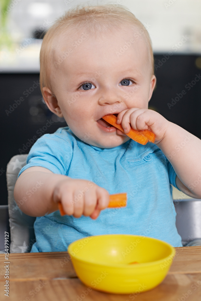 Happy Toddler Sitting At Table Eating Fresh Carrots Happy Toddler Sitting At Table Eating Fresh Carrots
