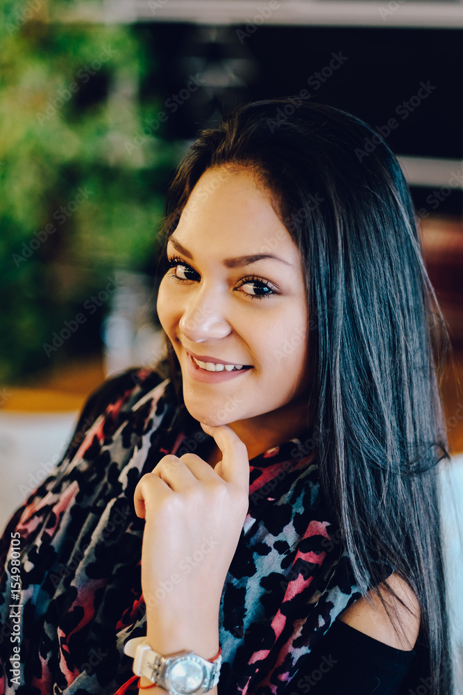 Naklejka premium Portrait of young dreaming girl in cafe. Beautiful girl sits in coffee shop and looks,Girl smiling, hand near face