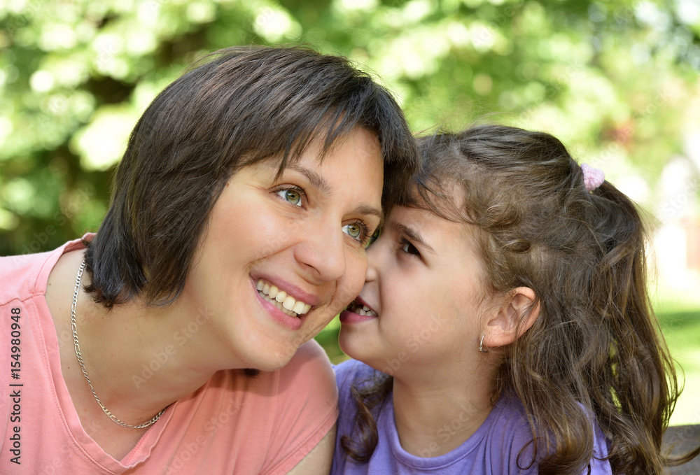 Daughter whispering secret into ears of smiling mother Daughter whispering secret into ears of smiling mother