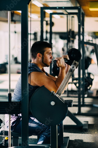 Attractive Young Man Doing Heavy Weight Exercise For Biceps On Machine In A Gym