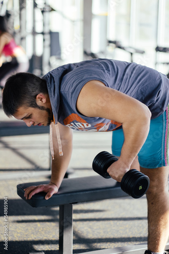 Young handsome man working out with dumbbells in a fitness gym