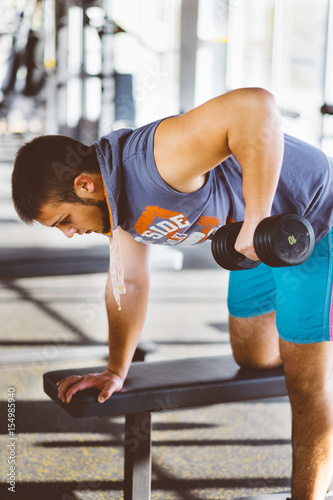Young handsome man working out with dumbbells in a fitness gym photo