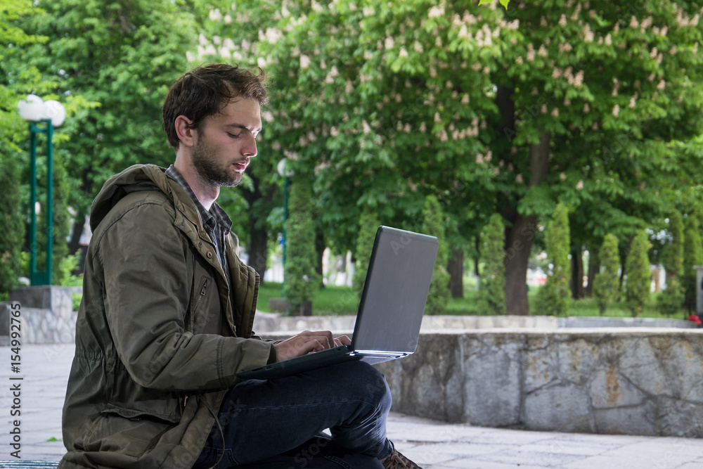 Young handsome student sitting on a wooden bench in the park with laptop computer. Young handsome student sitting on a wooden bench in the park with laptop computer.