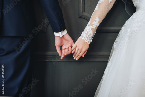Newlyweds hold hands. Grey background.