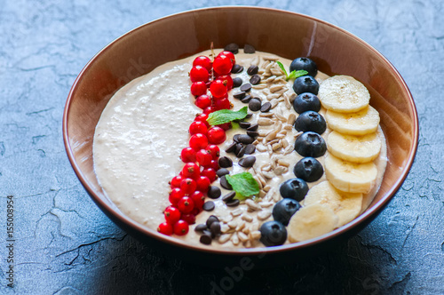 Super food smoothie bowl with oats, cootage cheese, milk, berries, sunflower seeds and banana on a black slate background. photo