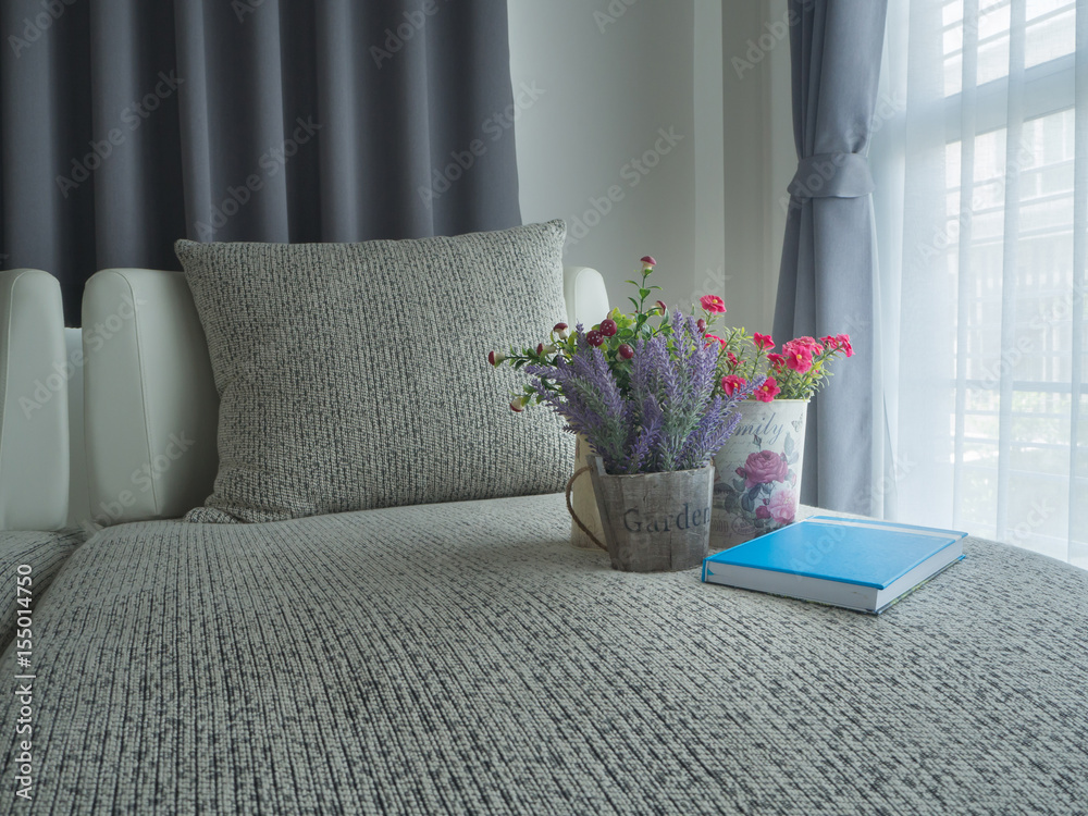 Φωτογραφία vintage sofa with variety colorful flower on pot and notebook paper blue cover on blurry beautiful white drape window texture background at bedroom