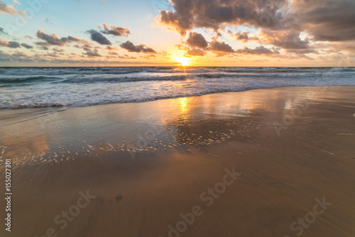 Ocean sandy shore with soft waves against sunrise sky on the background