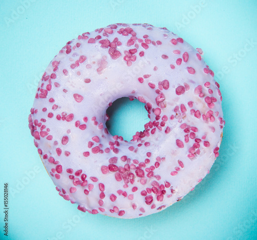 Glazed donut with colorful sprinkles on blue pastel background.