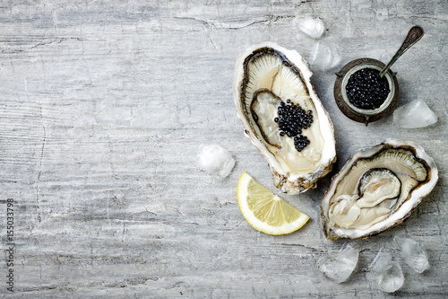Opened oysters with black sturgeon caviar and lemon on ice on grey concrete background. Top view, flat lay, copy space