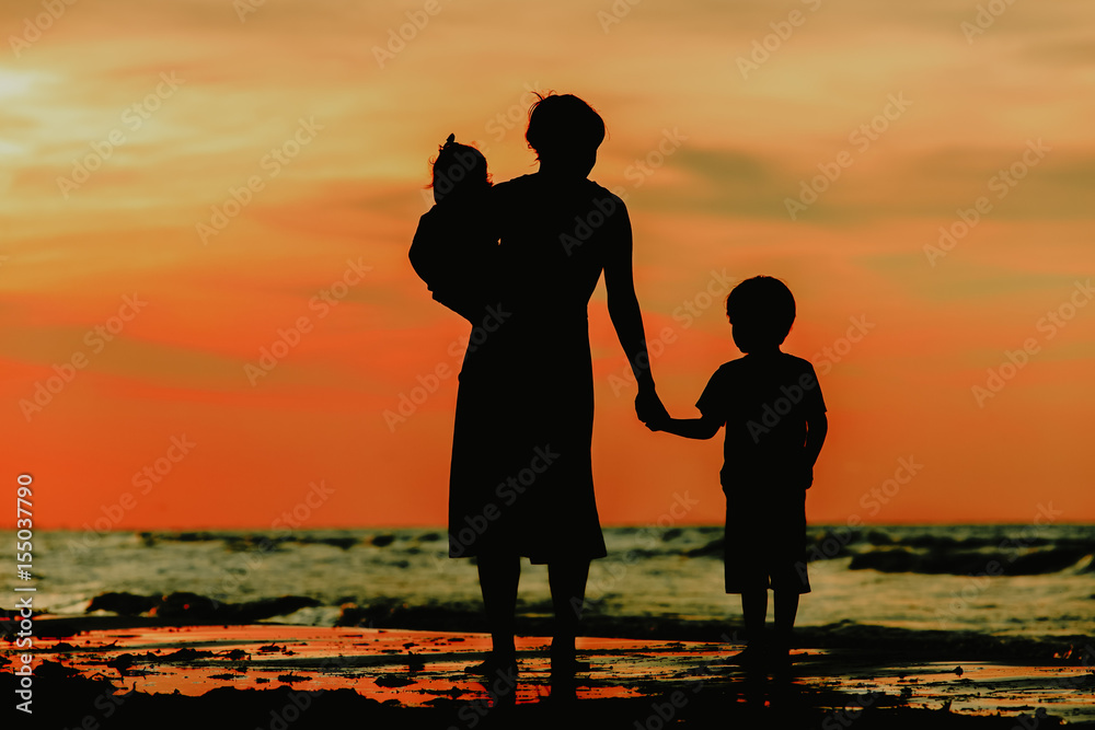 mother and two kids walking on sunset beach