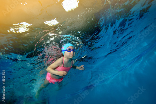 Little girl swims underwater in the pool on a background of lights in a pink swimsuit on a blue background. Portrait. Shooting under water. Horizontal orientation