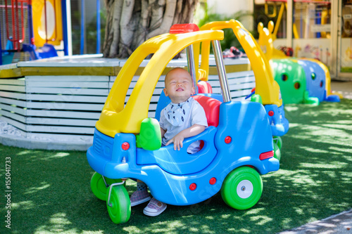Cute little Asian 1 year old toddler baby boy child riding on a colorful small toy car at play ground in the day time, Thailand, Kid first experience concept