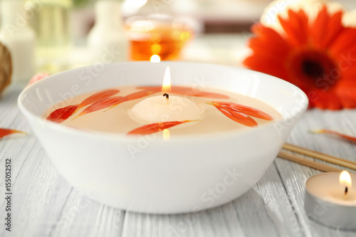Beautiful spa composition of flower petals and candle in bowl with water on table