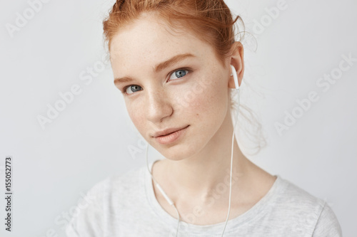 Ginger girl listening music in headphones looking at camera.